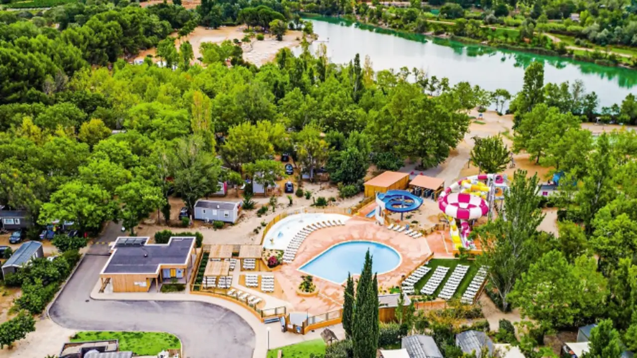 Vista a&eacute;rea de un camping 4 estrellas rodeado de naturaleza, con piscina, zonas recreativas y acceso directo a un r&iacute;o, ideal para unas vacaciones de relax y diversi&oacute;n al aire libre.