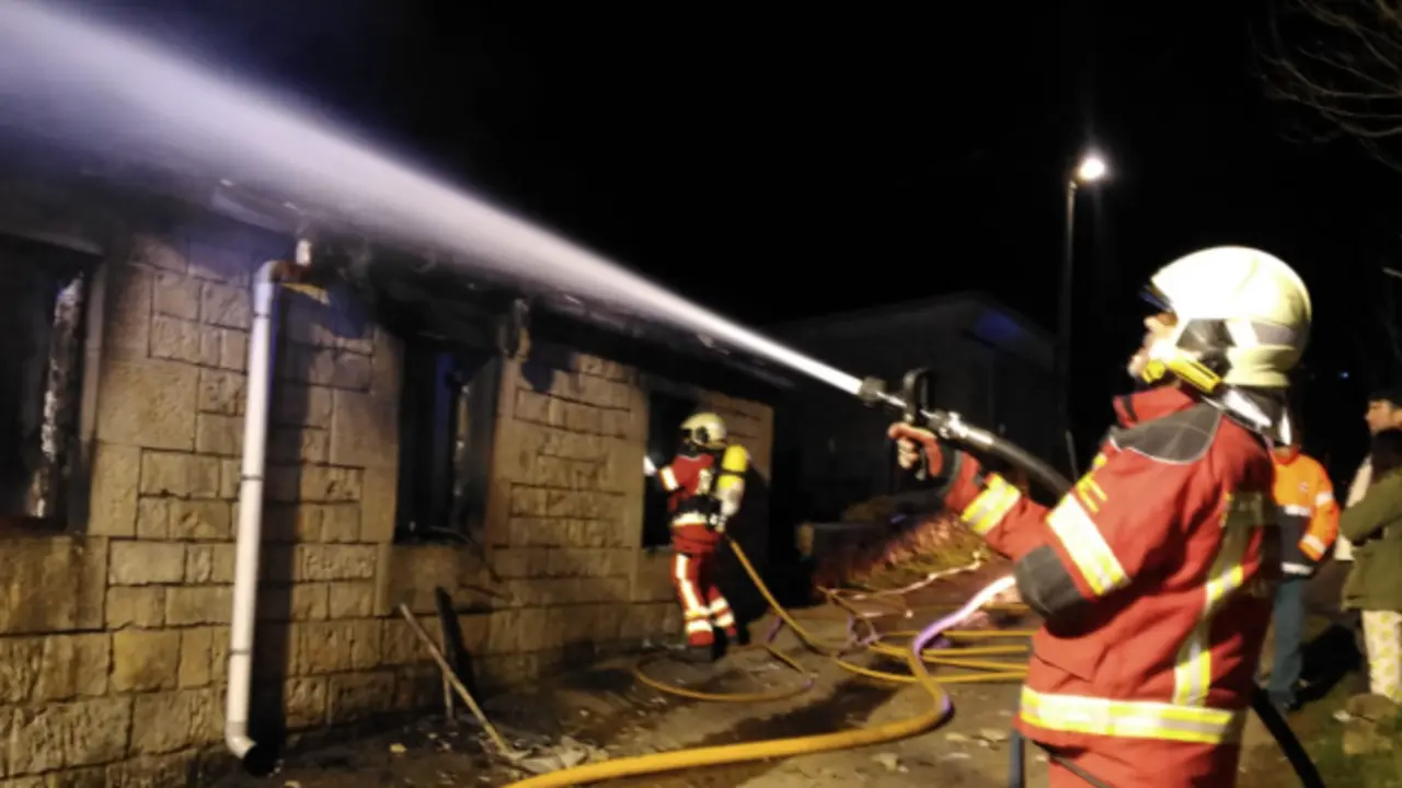 Un efectivo trabaja para sofocar las llamas en la caba&ntilde;a afectada en San Pedro del Romeral, mientras el fuego deja severos da&ntilde;os en la fachada y la cubierta del inmueble.