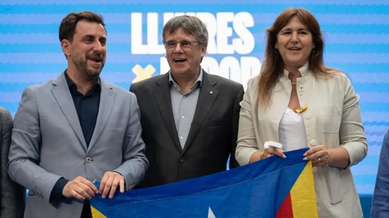 Toni Com&iacute;n (izquierda), Carles Puigdemont (centro) y una representante de Junts per Catalunya (derecha) posan con una estelada durant