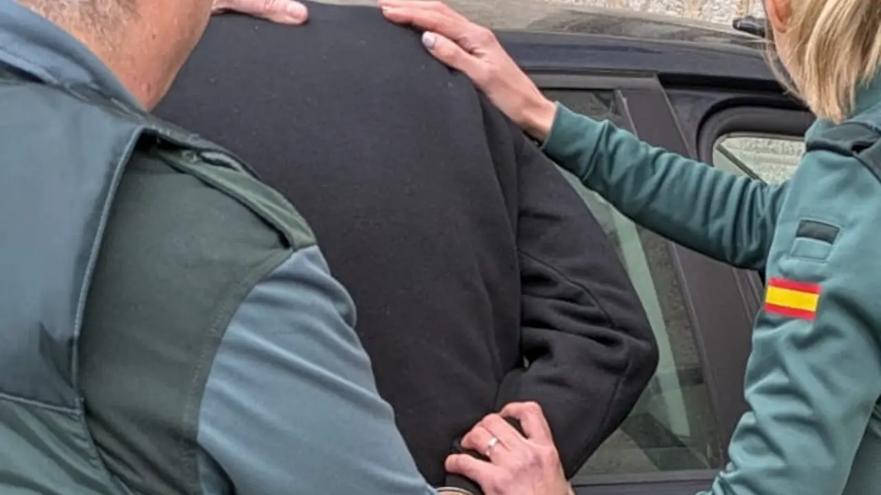 La imagen muestra a agentes de la Guardia Civil trasladando a un detenido. La persona arrestada, vestida con una sudadera negra, est&aacute; siendo sujetada por los agentes mientras le colocan las esposas. La escena se desarrolla junto a un veh&iacute;culo, lo que sugiere que el detenido est&aacute; siendo conducido a dependencias policiales. La imagen refuerza la seriedad del procedimiento y el protocolo seguido por las fuerzas de seguridad en