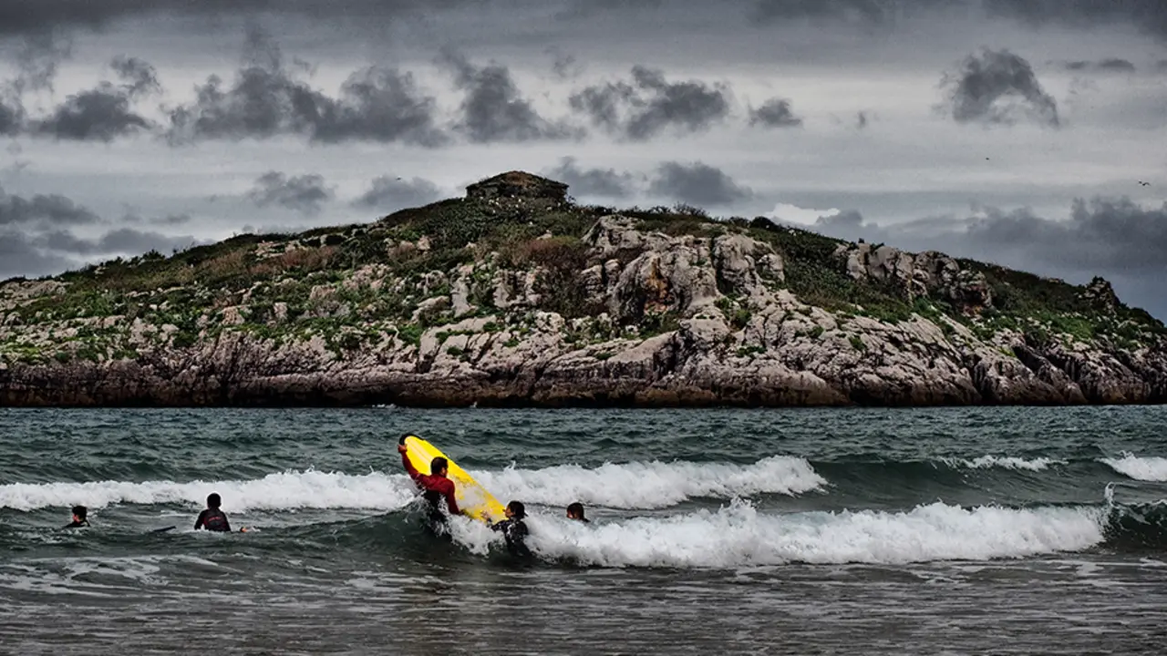 Vista de unos surfistas con la isla de San Pedruco en el fondo. / A.N.