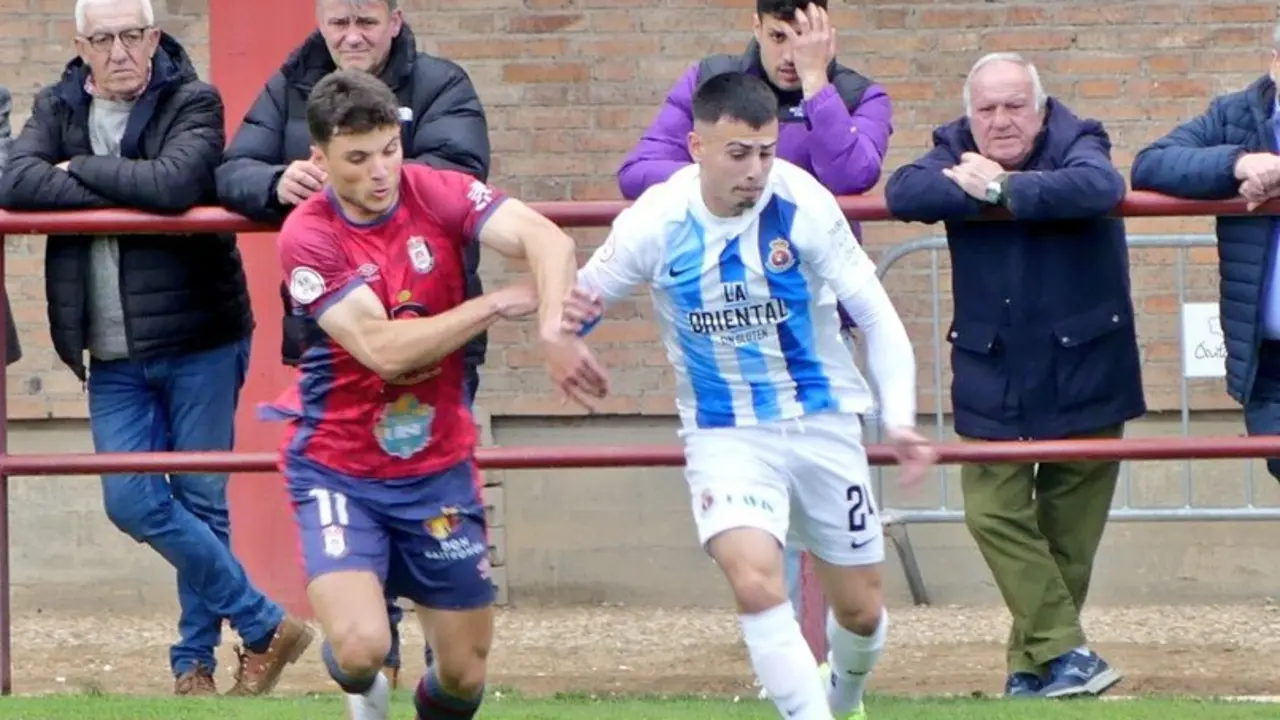 El jugador de la Gimn&aacute;stica intenta avanzar por la banda ante la presi&oacute;n de un rival del Real &Aacute;vila, en una acci&oacute;n del encuentro disputado en el Estadio Adolfo Su&aacute;rez, seguido de cerca por el p&uacute;blico desde la barandilla.