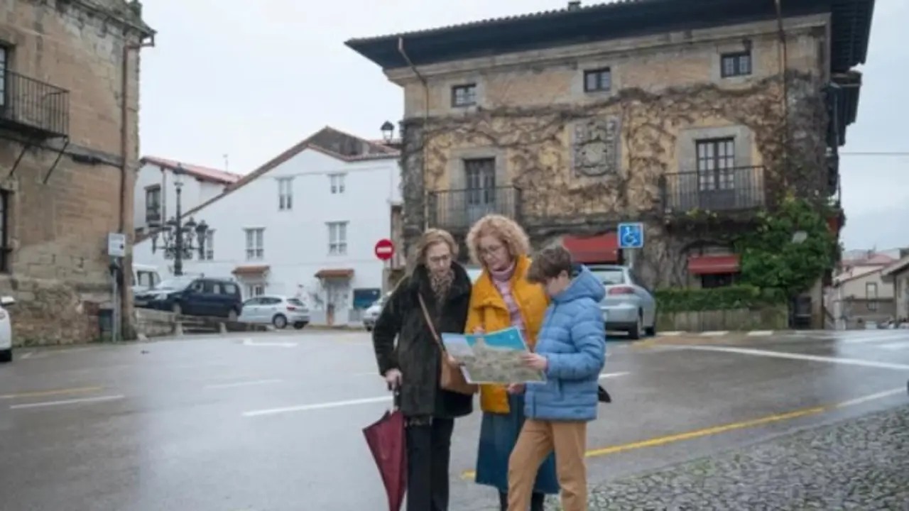 Tres visitantes consultan un mapa en el centro hist&oacute;rico de Santillana del Mar durante una jornada gris y h&uacute;meda en Cantabria.