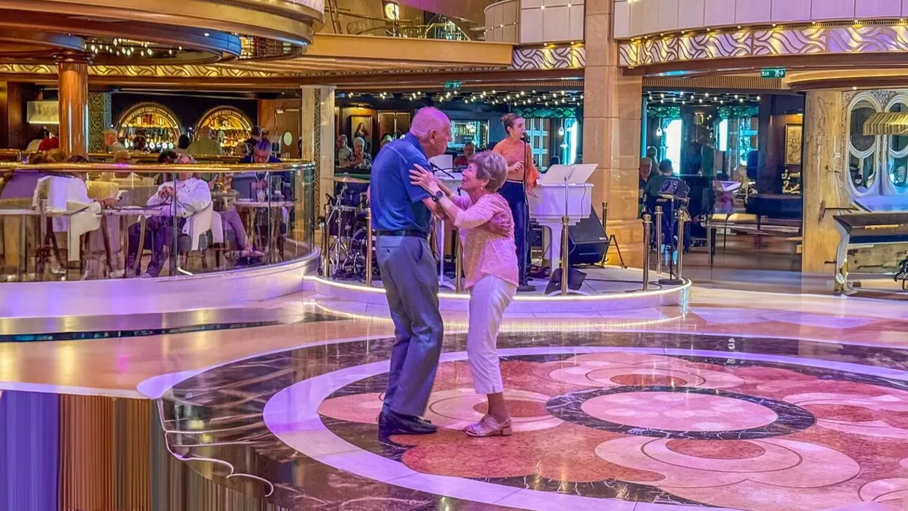 Pareja de adultos mayores disfrutando de un baile al ritmo de la m&uacute;sica en vivo, en un ambiente elegante y acogedor, probablemente a bordo de un crucero.