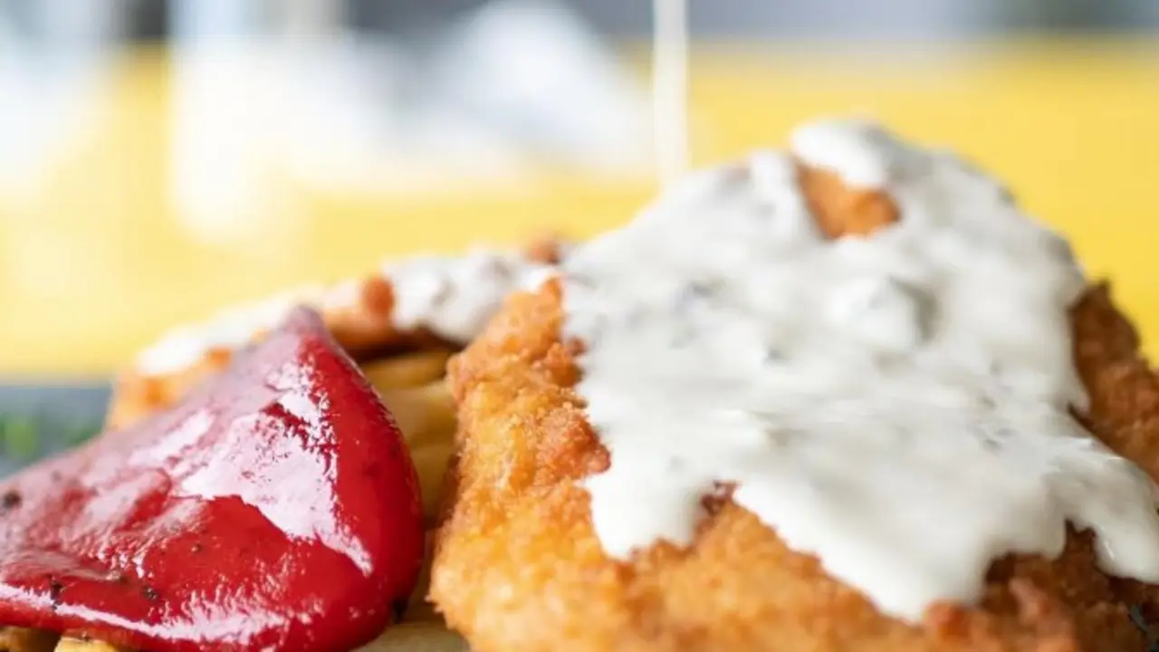 Salsa de queso cabrales sobre pechugas de pollo crujientes con patatas fritas, pimientos asados. / La Corbata