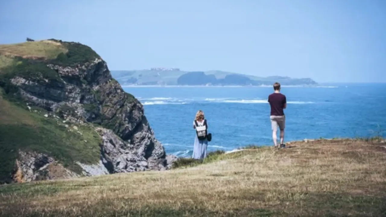 Dos turistas contemplan el mar Cant&aacute;brico desde un acantilado en la costa norte de Espa&ntilde;a, un destino cada vez m&aacute;s elegido por viajeros que buscan paisajes naturales, tranquilidad y temperaturas suaves durante el verano.
