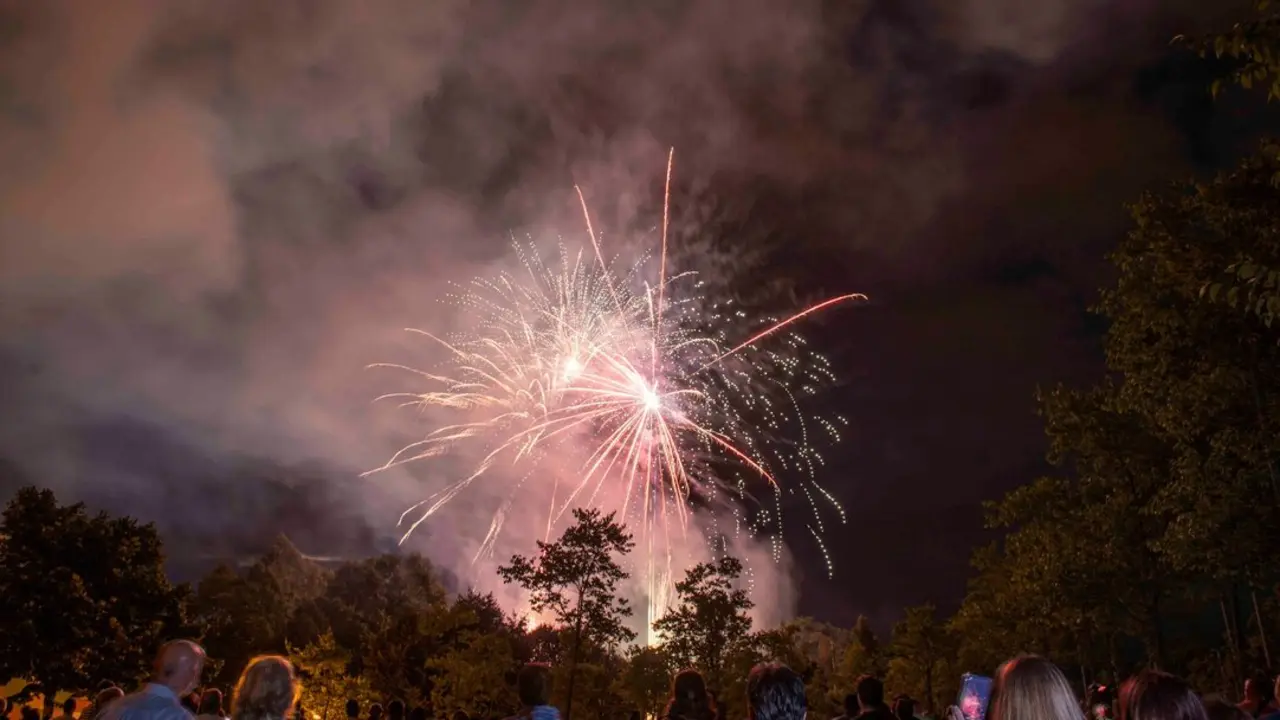 Espectadores contemplan el espect&aacute;culo de fuegos artificiales en una noche de celebraci&oacute;n bajo un cielo cubierto de humo y nubes.