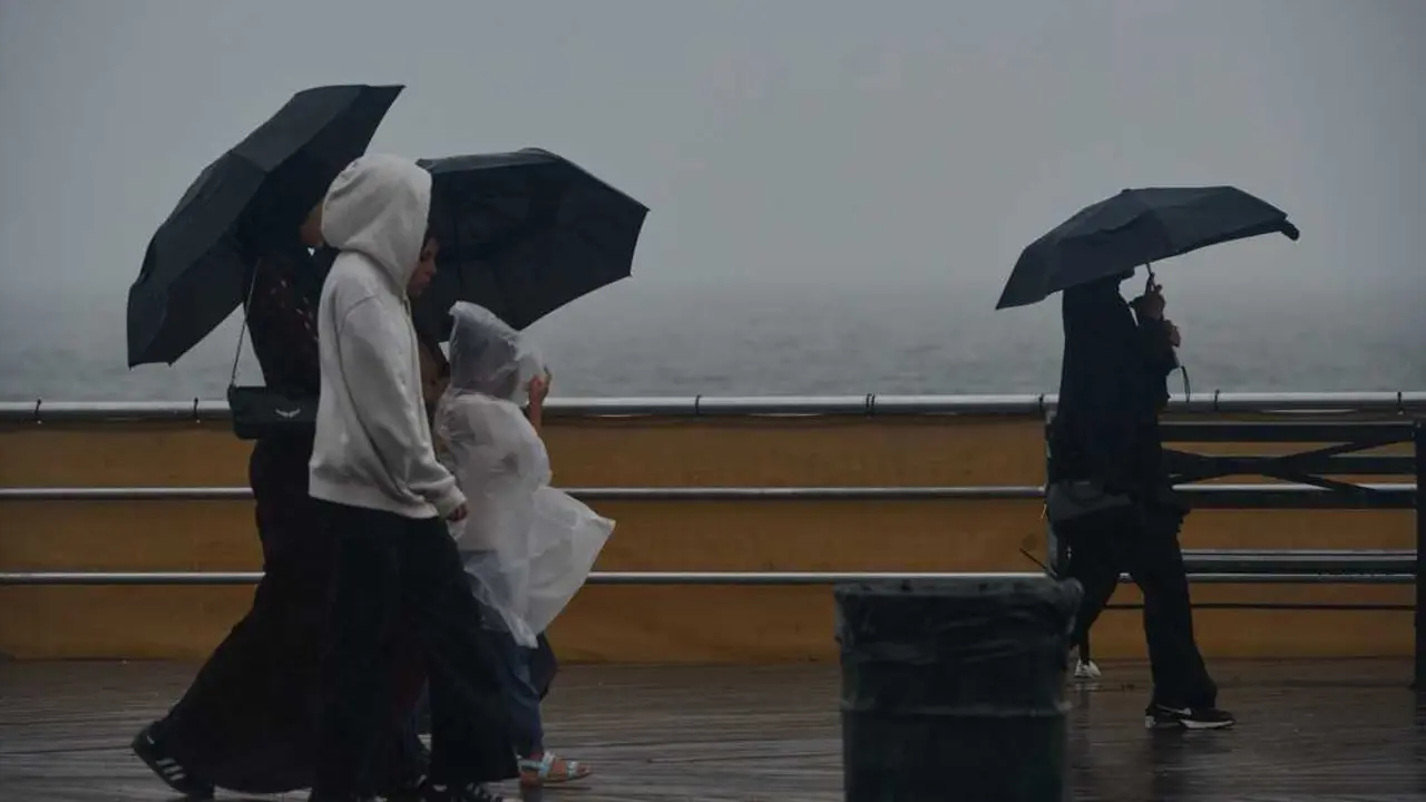 Varias personas pasean bajo la lluvia al lado de la playa. / Edna Leshowitz
