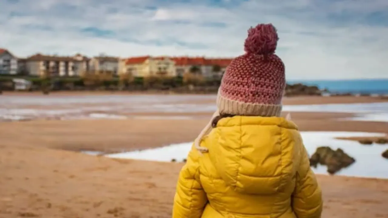Una ni&ntilde;a observa la playa en Cantabria en una jornada de cielos cubiertos y temperaturas suaves, t&iacute;pica del invierno.