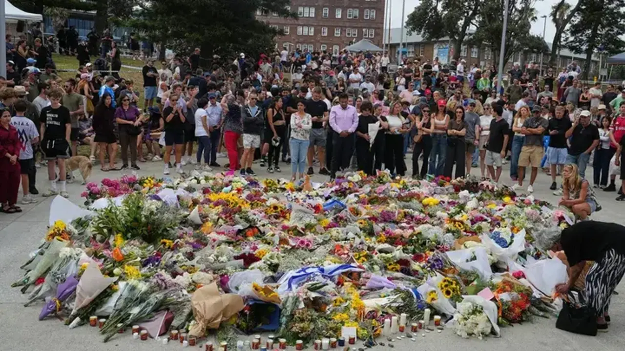 La gente se re&uacute;ne en torno a un homenaje a las v&iacute;ctimas del tiroteo frente al Bondi Pavilion en la playa Bondi de S&iacute;dney, el lunes, un d&iacute;a despu&eacute;s de la masacre. (Mark Baker/The Associated Press)