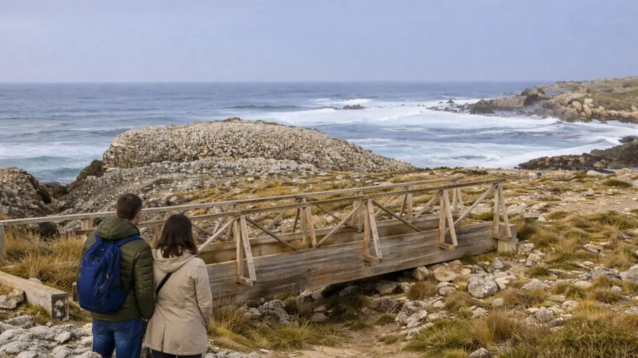Dos curiosos observan el oleaje desde la izquierda del puente, contemplando la fuerza del mar en la costa rocosa.