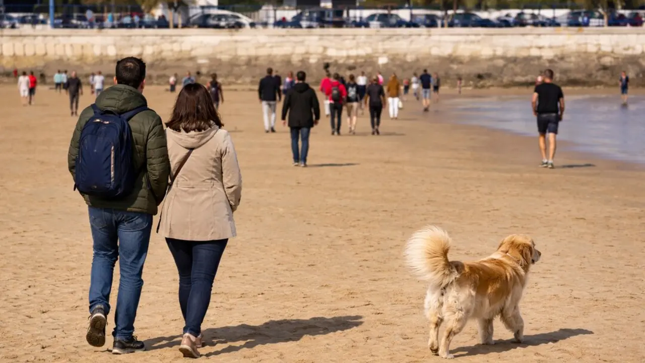 Varias personas pasean por la playa de Santander en una jornada soleada, disfrutando del buen tiempo en la costa.