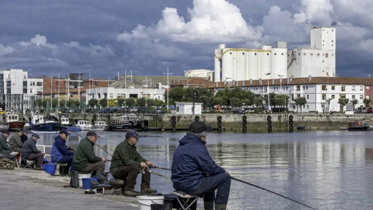 Varios pescadores disfrutan de una jornada tranquila junto al agua en el Barrio Pesquero de Santander, bajo un cielo cubierto que anticipa cambios de tiempo.