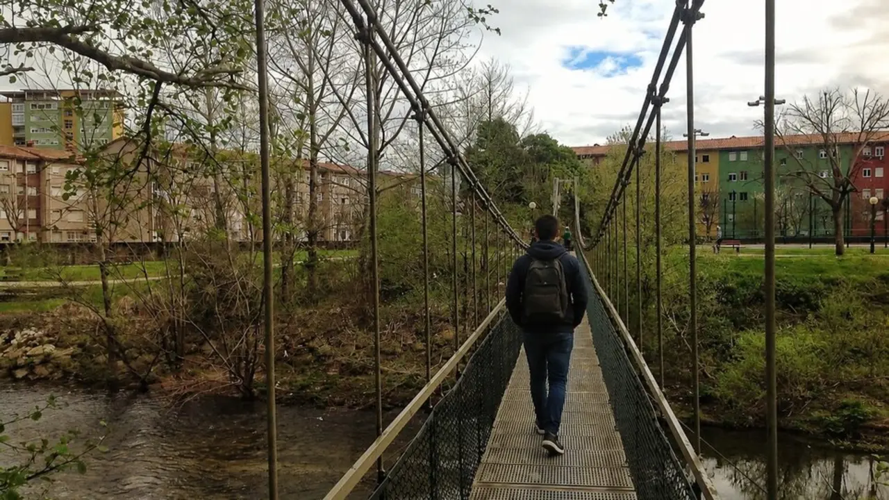 Una persona cruza el puente colgante del parque de La Viesca, una de las infraestructuras peatonales m&aacute;s emblem&aacute;ticas de este espacio natural situado entre Torrelavega y Cartes, muy frecuentado por senderistas, ciclistas y paseantes.