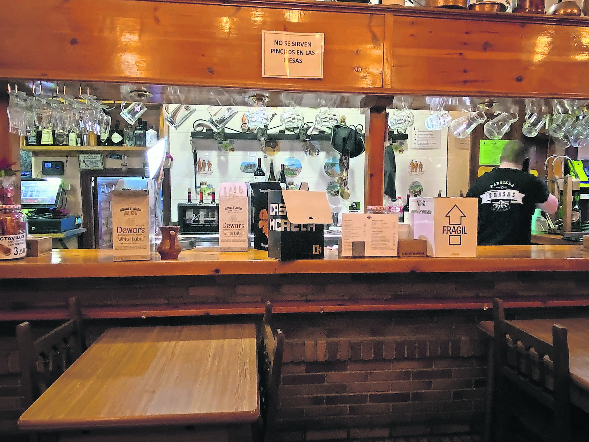 Trabajador de un bar atiende al teléfono, mientras repone las bebidas. / Lucio V. del Campo