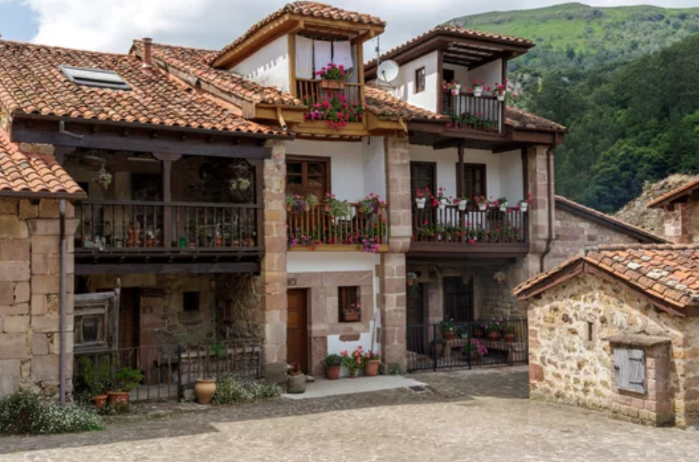 Encantadoras casas montañesas en Carmona, Cantabria, con sus tradicionales balcones de madera adornados con flores, tejados de teja roja y muros de piedra que reflejan la esencia de la arquitectura rural cántabra en un entorno de naturaleza y tranquilidad.