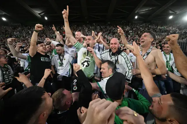 Un futbolista del Racing celebra el ascenso con una bandera verdiblanca mientras El Sardinero corea el regreso a Primera División.