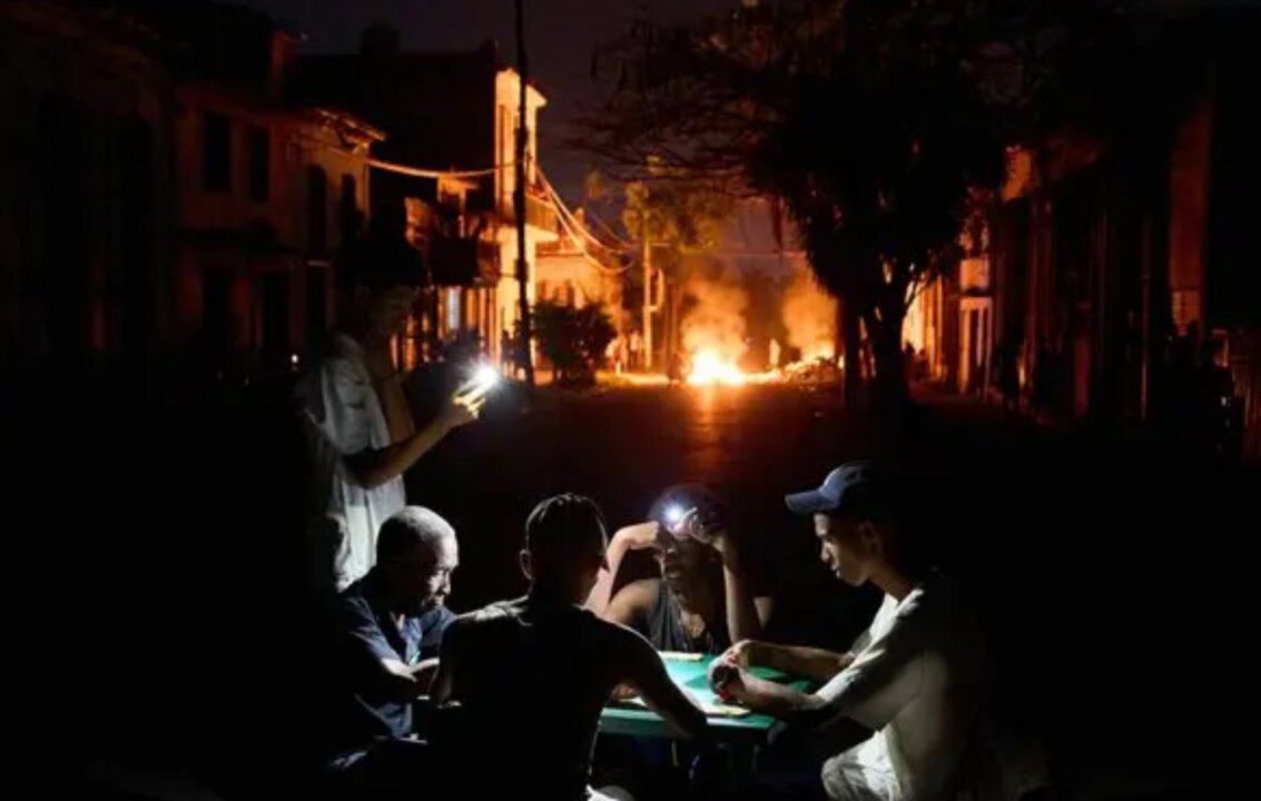 Cubanos juegan al dominó iluminados con teléfonos móviles durante un apagón en La Habana, mientras una hoguera arde al fondo en señal de protesta por la crisis energética.